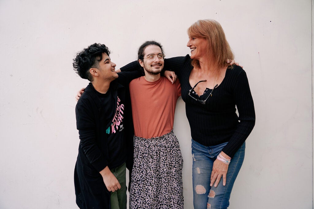Three Trans*Lounge staff members, smiling candidly, pose with arms around one another.