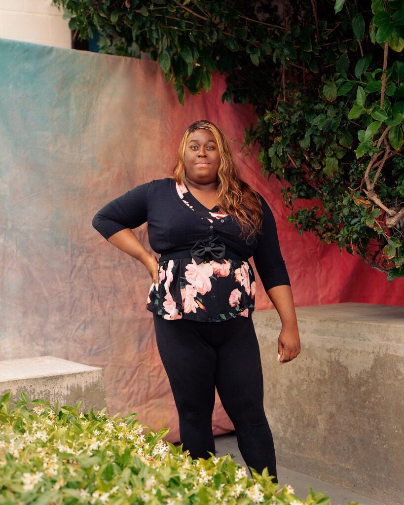 Black trans woman who works at the Center, standing outdoors in front of a rainbow ombre backdrop