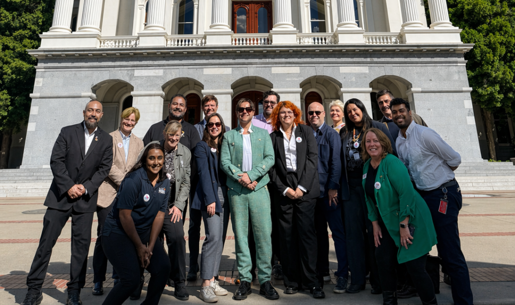 A group of people, dressed up in business casual wear, posing for a photo in front of the California State Capitol. The sky in the background is blue.