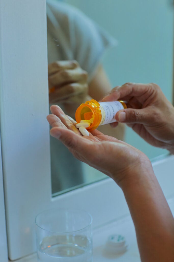 A male-identified person's hands holding a pill bottle, with one white pill coming out of it.